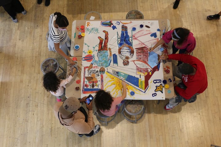 An overhead photo of 6 adults and children working on a painting together